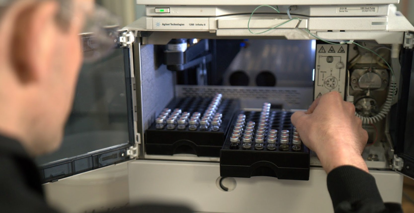 Scientist loading sample vials into laboratory analysis equipment for custom chemical synthesis testing.